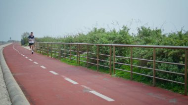 Motivasyonlu koşucu şehir yolunda koşuyor. Profesyonel atlet eğitimi sabah koşuyor. Koşan yakışıklı esmer dışarıda kulaklık takıyor. Formda sporcu sokakta kardiyo dayanıklılık egzersizi yapıyor..