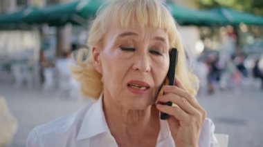 Sunny caddesinde konuşan ciddi bir emekli. Kapatın. Dışarıdaki kafeteryadan akıllı telefon arayan endişeli yaşlı kadın. Seçkin emekli kadın telefon konuşmasında sorun yaşıyor..