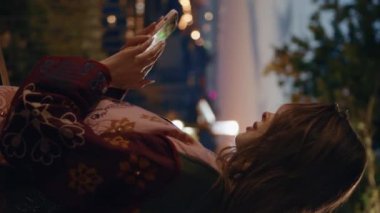 Akıllı telefonlu, karanlık şehir gözlem güvertesinde duran bir bayan. Gecenin karanlığında cep telefonu yazan rahat bir kadın dikey olarak alacakaranlıkta. Gece geç saatlerde dışarıda cep telefonuyla mesajlaşan kız..