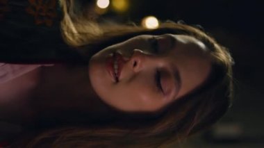 Karanlık sokakta yürüyen bir kadın boş gece kasabasının tadını çıkarıyor. Çekici bir kadının gece yarısı şehirde gezinen portresi dikey video. Lüks, rahat, gülümseyen bir kamera. Şehir eğlencesi..