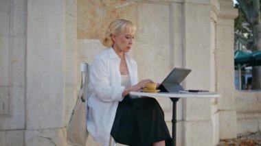 Kafe terasında dizüstü bilgisayarda e-posta yazan yaşlı kadın. Uzaktan kumandalı açık hava restoranında çalışan ciddi emekli iş kadını. Zarif olgun kadın klavyedeki tablet ekran yazı metnine odaklandı.