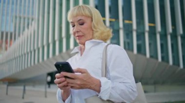 Akıllı telefonlu internet sörfü yapan yaşlı bir iş kadını. Şehir içi iş caddelerini kapatıyor. Açık havada cep telefonunda kendine güvenen olgun yönetici tarama uygulaması. Başarılı bir yaşlı kadın cep telefonu mesajlaşması