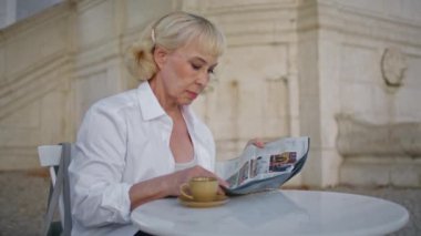Restoranın terasında yaşlı kadın dergisi var. Ciddi, yaşlı bir kadın kafeteryadaki açık havada günlük makalesi okuyor. Zarif, olgun bir bayan sabah baskısının tadını çıkarıyor..