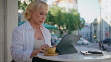 Emekli iş kadını şehir restoranında tablet üzerinde çalışıyor. Kendine güveni tam yaşlı bir kadın dışarıda, kafeteryada bilgisayar başında oturuyor. Havalı zengin emekli kablosuz cihaz ekranı görünümlü