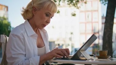 Büyükannem dışarıdaki kafe masasında bilgisayar kullanmakla meşgul. Olgun kadının kafası karışık, tablet ekranda açık hava restoranında oturuyor. Laptop klavyesinde yazı yazan zarif yaşlı kadın..