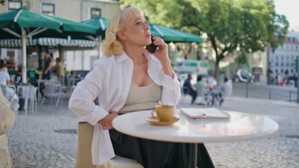 屋外のカフェテーブルで携帯電話を話す成熟したビジネスマン レストランのテラスで電話で指示を与える自信のある女性の上司 携帯電話を話すよく成長した老婦人 — ストック動画