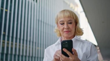 Kırışık kadın akıllı telefonları kaydırıyor. Şehir caddesinde yürüyor. Yaklaş. Go iş bölgesinde cep telefonu başvurusu yapan gülümseyen olgun bir kadın. Zarif mutlu emekli cep telefonundan mesaj okuyor.