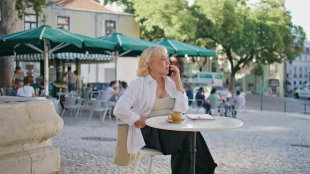 屋外のシティカフェで携帯電話をかけている豪華な上級女性 オープンエアレストランだけに座っているスマートフォンを話すエレガントな老婦人 心配している高齢女性は路上で深刻な電話会話を持っています — ストック動画