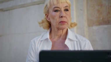 Sokakta dizüstü bilgisayarda çalışan yaşlı bir kadın. Dışarıdaki bilgisayar ekranına odaklanmış yaşlı kadın portresi. Zengin başarılı emekli, tablet e-posta okuyarak şehir kafesinde oturuyor.