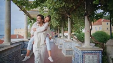 Akdeniz balkonunda kadını sırtında taşıyan gülümseyen bir adam. Mutlu çift yaz parkında romantik bir buluşmada eğleniyor. Mutlu çift, mutluluğu hissediyor. Üzüm çalılarının arasında geziniyor. 