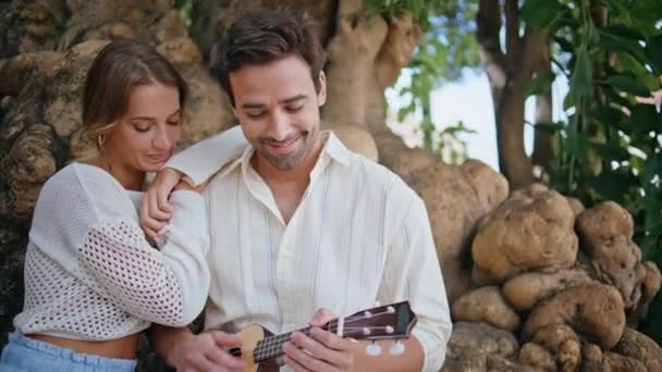 喜爱情侣们在夏季公园的特写中欣赏音乐 松懈的音乐家 在大自然中弹奏吉他 触动琴弦 笑着的夫妻依偎在树林里放松地在一起 浪漫的结婚纪念日 — 图库视频影像