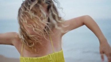 Sahilde dans eden etkileyici bir kız. Yakın plan. Profesyonel kadın koreograf, doğaya tutkuyla bağlı esnek bir vücudu hareket ettiriyor. Muhteşem kıvırcık kadın deniz kıyısında tek başına dans ediyor..