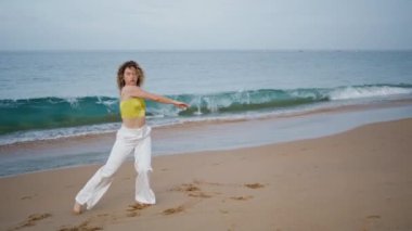 Dansçı, okyanus dalgalarının önünde çağdaş koreografi pratiği yapıyor. Kum sahilinde dans eden enerjik kıvırcık kadın modern dans gösterisi yapıyor. Bedenini deniz kıyısında hareket ettiren profesyonel sanatçıya ilham verdi.