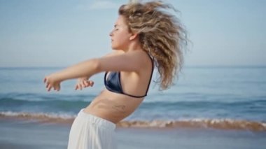 Güzel okyanus kıyısında çağdaş dans pratiği yapan seksi kadın. Yakın çekim. Beyaz etek giyen kıvırcık kız tahrik edici bir şekilde hareket ediyor. Modern koreografiyi sergileyen şehvetli kadın sanatçı..