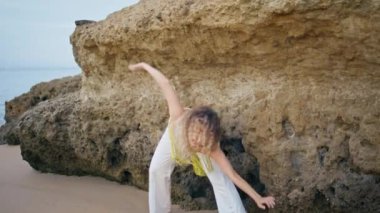 Çağdaş kız, kayalık sahil bükücü esnek vücutla dans ediyor. Kum plajında modern koreografiyi icra eden yetenekli profesyonel dansçı. Güzel kadın sanatçı doğada abartılı danslar yapıyor..