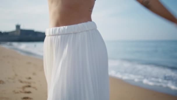 夏の夏に海岸を歩く見知らぬ女の子が閉まりました 砂浜で踊る白いスカートの未知の若い女性は幸せを感じます スリムな入れ墨の女性は美しい海岸で落ち着いた散歩を楽しむ — ストック動画