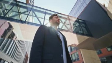 İş yeri sahibi yaz güneşinin altında caddede dikiliyor. Modern ofis binasının yakınında poz veren kendinden emin genç bir lider. Mesafeye bakan başarılı bir girişimci. Kamera hareket ediyor.