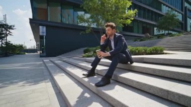 Rahat Ceo konuşan cep telefonu kahve fincanı yakınlaştırmalı şehir merdivenlerinde oturuyor. Kendine güvenen zarif iş adamı iş meselelerini uzaktan çözüyor. Yakışıklı adam güneşli caddede telefon görüşmesi yapıyor.