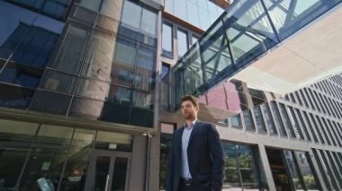 Şık bir bankacı tek başına şehir ticaret bölgesini poz vererek yakınlaştırıyor. Güneşli bir günde ofis binasında duran yakışıklı, kendine güvenen bir iş adamı. Başarılı CEO sokak güneşine bakan bir kamera.