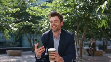 Kahve işadamı Sunny Caddesi 'ndeki akıllı telefondan gülüyor. Happy, cep telefonu park yerinde sosyal medyayı izleyerek rahatladı. Tasasız menajer dışarıda mola vermeyi sever..