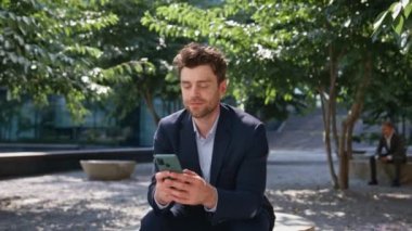 Green Park 'a yakın oturan akıllı telefondan mesaj okuyan gülümseyen adam. Mola yerinde cep telefonuyla mesaj atan mutlu yakışıklı iş adamı. Şık tıraşsız menajer güneşli meydanda buluşma ayarlıyor.