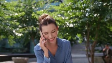 Neşeli iş kadını elinde kahve fincanıyla cep telefonuyla konuşuyor. Gülümseyen kadın, akıllı telefondan arıyor Sunny City Park 'ta oturmuş içecek servisi yapıyor. Kadın yönetici iş molası.