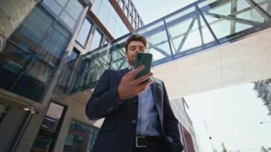 Güneşli sokak manzarasında kendine güvenen girişimci cep telefonu ekranı. Şık iş adamı telefon mesajı okuyor. Şehir merkezinde duruyor. Yakışıklı şirket sahibi dışarıda akıllı telefon uygulamasına bakıyor..