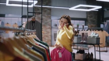 Alışveriş meraklısı, akıllı telefondan arıyor ve alışveriş merkezinin kapısından kıyafet seçiyor. Mağazada yürüyen mutlu duygusal bayan müşteri butik merkezinde yeni moda koleksiyonu arıyor. Alışveriş konsepti