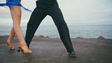 Dansçı bacakları kasvetli kıyıda profesyonel olarak hareket ediyor. Bilinmeyen tutkulu sanatçılar ayaklarıyla enerjik dans hareketleri yapıyorlar. Partneriyle dans eden baştan çıkarıcı kadın bulutlu sahil ağır çekim