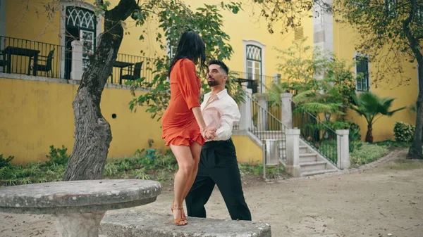 Two professional dancers performing hot salsa on street. Elegant man lifting up beautiful woman partner dancing latino choreography in park. Passionate energetic artists moving sensually slow motion.