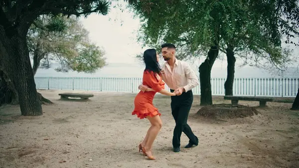 Couple young professional dancers dancing in city park summer day. Elegant woman brunette in red dress spinning in man hands. Sensual pair performing salsa slow motion. Happy partners moving together.