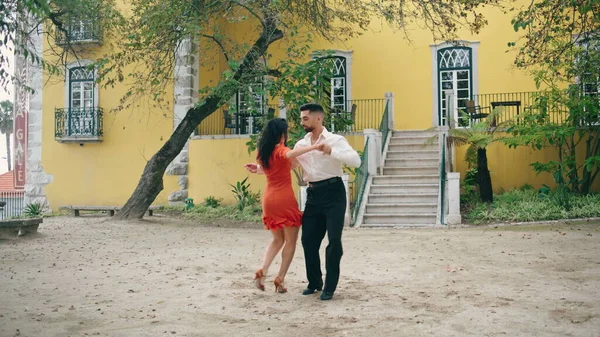 Happy couple dancers performing energetic dance on street. Two professional passionate performers dancing latino style slow motion. Sensual brunette woman enjoy performance with elegant hispanic man.