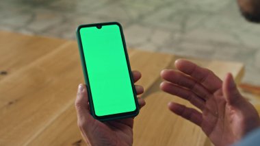 Kapalı alandaki yeşil ekranlı telefondan konuşan el kol hareketi yapan adam. Kimliği belirsiz bir avukatın sıcak ışık ofisindeki Chromakey akıllı telefonu araması videosu. Yetişkin yönetmen el hareketleriyle ekrandaki telefon görüntülerini düzenliyor.