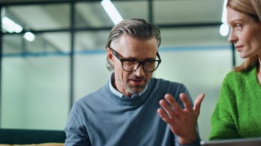 Konferans odasında yakın çekimde tartışan mutlu meslektaşlar. Sakallı işadamı, el kol hareketleri yapan sarışın iş kadını dikkatle dinliyor. İki zeki ortak iş anlarını çözmek için beyin fırtınası yapıyor.