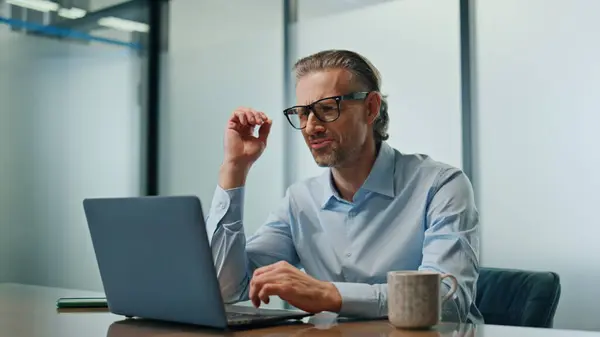 Angry businessman feeling stressed at workplace closeup. Aggressive entrepreneur disappointed failure looking laptop at office interior. Nervous man taking off glasses checking information at computer