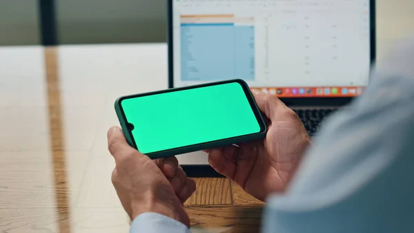 Boss fingers hold mockup cellphone at office closeup. Anonymous leader man watching green screen template device. Unknown ceo looking chroma key phone resting at table. Financial analyst reading news
