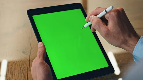 Artist hand drawing stylus on chromakey tab display closeup. Creative business man fingers using electric pen on green screen tablet computer. Unrecognizable designer working mockup pad in office desk