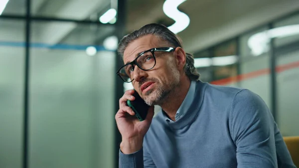 Portrait successful businessman calling partner indoors. Happy stylish employee talking cellphone in lobby zone. Confident unshaven financial manager discussing business deal at corporate office couch