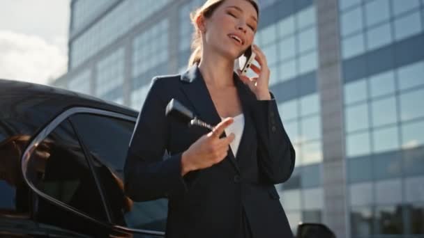 成功的汽车销售员在街上叫卖 手里拿着钥匙 把镜头放大 快乐的女商人一边说着智能手机一边靠着高档汽车 优雅的女士汽车采购员会讲手机 — 图库视频影像