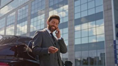 Tatmin olmuş iş adamı araba anahtarlarıyla oynayan akıllı telefonları yakınlaştır. Gülümseyen sakallı patron, lüks araba satın alma haberlerini paylaşmak için arıyor. Mutlu zengin adam telefonda iş başarısını tartışıyor..