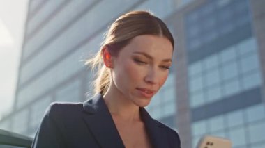 Güneşli iş bölgesinde cep telefonu daktilo eden güzel bir bayan. Kapatın. Zarif bir iş kadını akıllı telefonların durduğu caddeye odaklandı. Çekici kadın CEO Yöneticisi şehir merkezinde telefonla mesajlaşıyor..