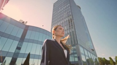 Zengin kadın yaz güneşinde şehir merkezinde poz veriyor. Güzel başarılı iş kadını modern şehir gökdelenlerinin önünde tek başına duruyor. Zarif bir bayan dışarıdaki objektife bakıyor. Kamera hareket ediyor.