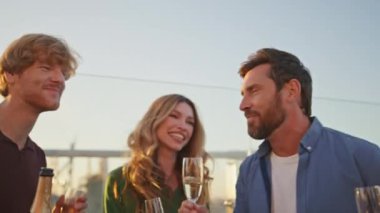 Heyecanlı arkadaşlar güneşli çatıda eğleniyor. Çeşitli insanlar ellerinde şampanya bardaklarıyla akşam güneşinde dans ediyorlar. Neşeli arkadaşlar yazın dışarıda eğleniyorlar..