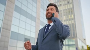Gülümseyen işadamı şehir caddesinde yürüme işini bitirdi. Mutlu başarılı yönetici akıllı telefonu kapattı. Dışarıdaki kameraya bakıyor. Neşeli iş adamı telefon konuşmasından memnun..