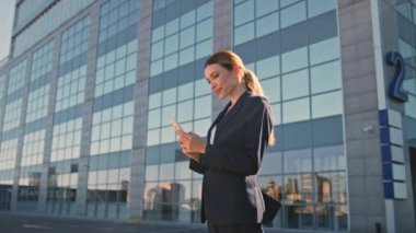 İş kadını ofis kapandıktan sonra dışarıda telefonda SMS okuyor. Harika bir bayan yönetici ayakta duran akıllı telefonu kaydırıyor. Zengin kadın girişimci görünümlü cep telefonu ekranını yakınlaştır
