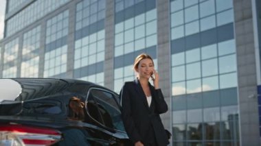 Gülümseyen bayan patron cep telefonunu arıyor. Lüks arabaya yaslanıyor. Yaklaş. Güzel, rahat iş kadını ofis binasının yakınındaki akıllı telefonu arıyor. Mutlu kadın CEO 'lar telefonla başarılı bir pazarlığa giriyorlar.