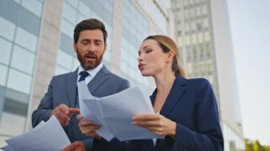 Şehir merkezindeki yakın planda sözleşmeyi tartışan yürüyen ortaklar. Gülümseyen iş ortakları iş belgelerini dışarıda okuyorlar. Mutlu şirket meslektaşları sokakta kağıt anlaşması hakkında konuşuyor.