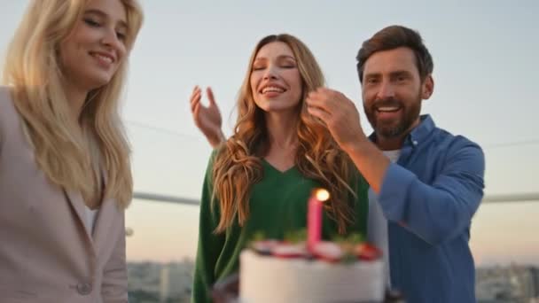 在屋顶派对上 朋友们把生日蛋糕带给笑容可亲的女人 兴奋的女孩和伴侣一起吹点蜡烛庆祝结婚周年 笑着在智能手机上给自己带来惊喜的朋友 — 图库视频影像