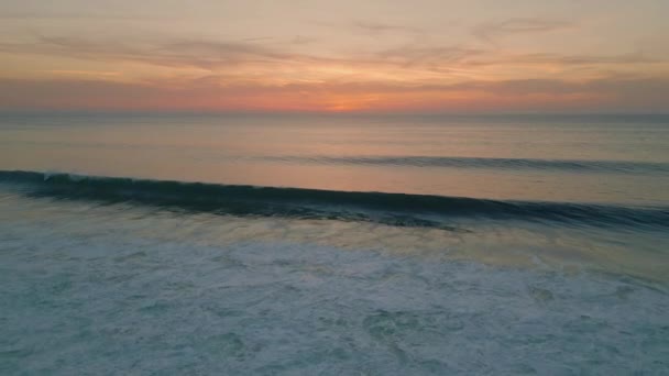 トランキル夏の海の日の出の空中ビュー 深い暗い海の表面上の雄大なオレンジ色の空 スーパースローモーションで海岸に転がる美しい泡立った波 休暇中の美しい海洋の朝 — ストック動画