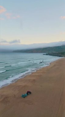 Dikey fırtınalı okyanus sörfü köpüklü kum dronu görüntüsü. Deniz suyu dalgaları kumlu plaj arabalarını yıkıyor ve kum üzerinde çok yavaş hareket ediyor. Deniz kıyısında sığ sularla kaplanmış sinematik beyaz sprey.